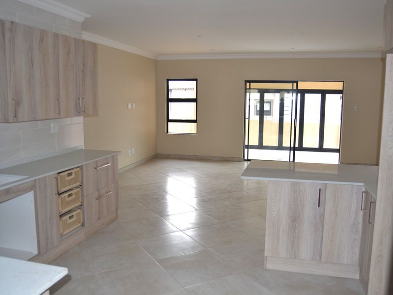 Spacious open-plan kitchen and living area featuring modern light wood cabinetry, stone countertops, tiled floors, and large sliding doors leading to the exterior.