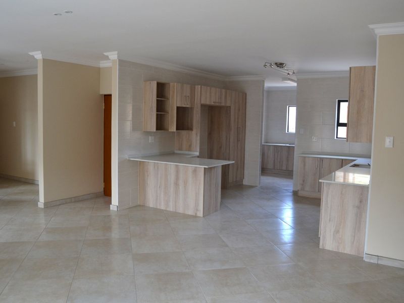 Spacious open-plan kitchen area featuring modern light wood cabinetry, stone countertops, and neutral tiled flooring throughout.