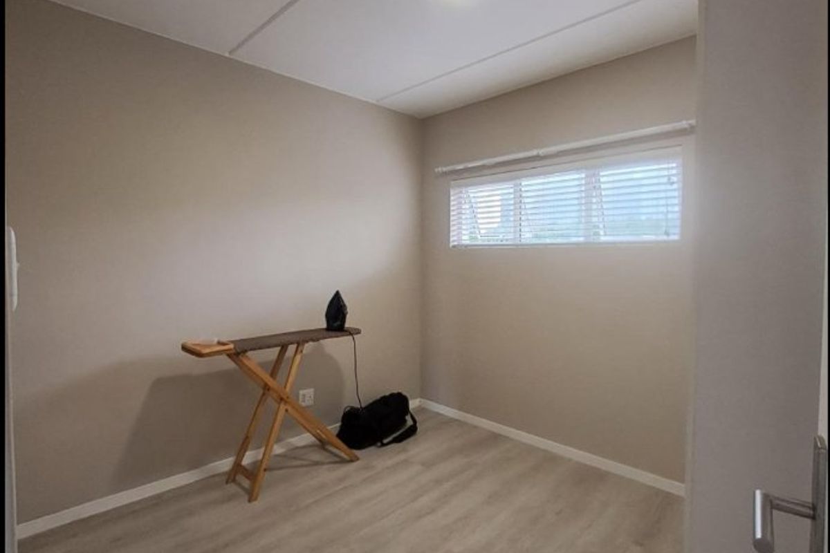 A clean, neutral-toned bedroom featuring modern laminate flooring, recessed ceiling lighting, and horizontal window blinds, offering a bright and versatile living space.