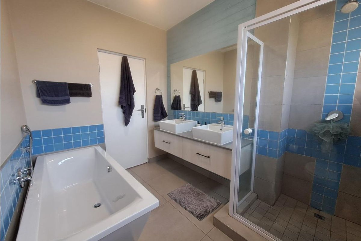 Modern bathroom featuring a double vanity with vessel sinks, a separate glass-enclosed shower, and a built-in bathtub with blue tiled accents.