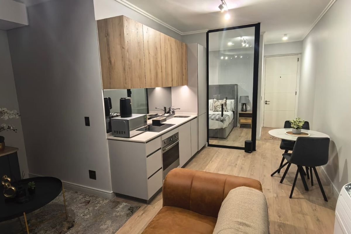 Modern open-plan apartment featuring a compact kitchen with wood-finish cabinetry, integrated appliances, and a stylish glass partition separating the living and sleeping areas.