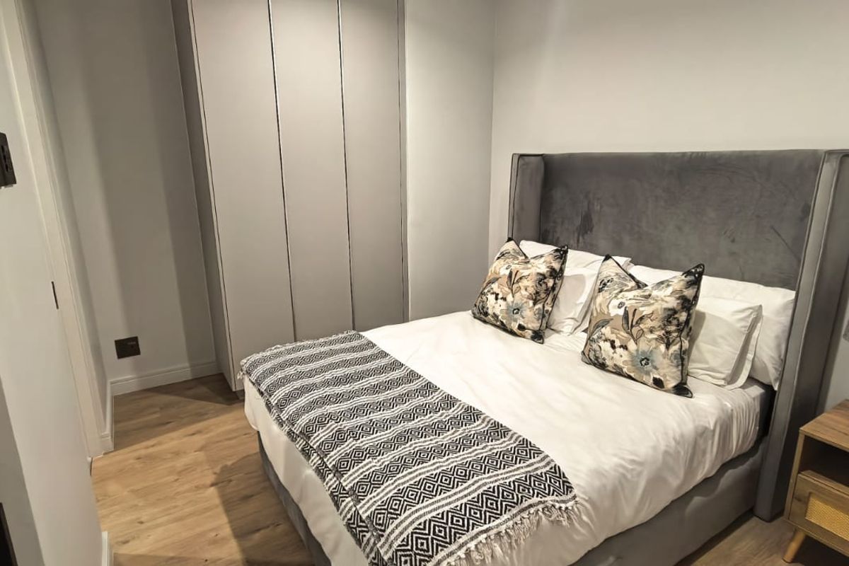 A modern bedroom featuring light laminate flooring and a floor-to-ceiling built-in wardrobe with a neutral finish.