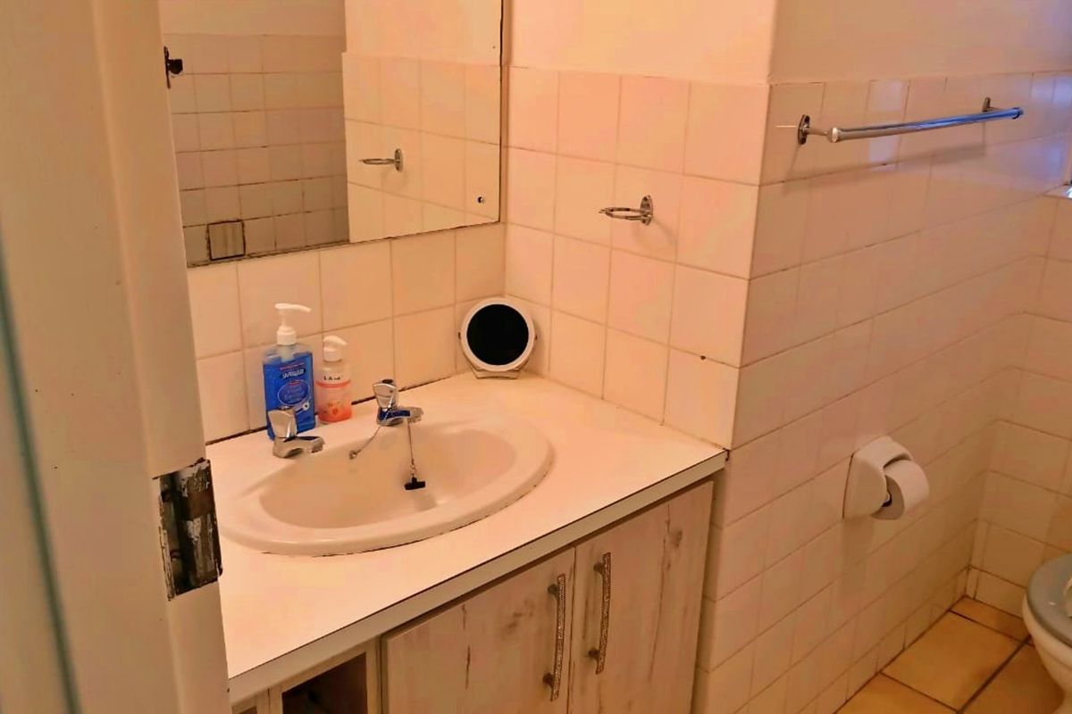 A dated bathroom featuring a vanity cabinet with a ceramic basin, wall-mounted mirror, and standard toilet, finished with ceramic wall and floor tiles.