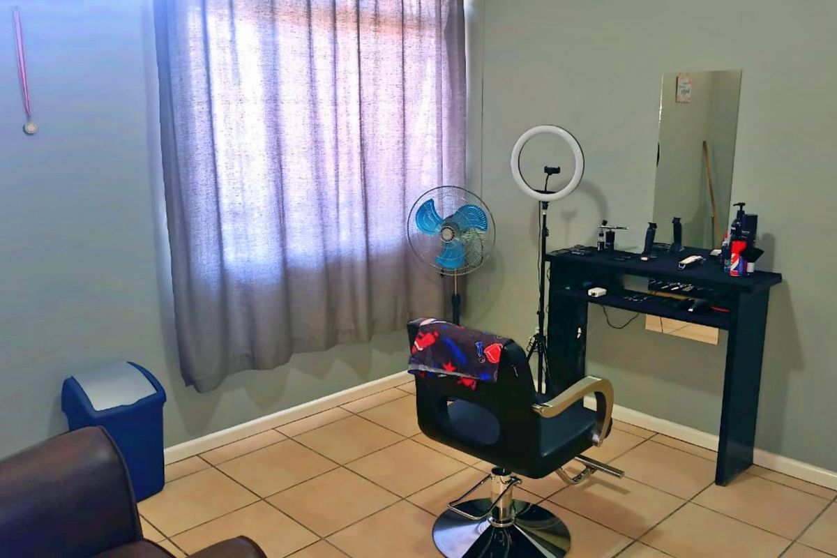 A bedroom space currently utilized as a salon, featuring tiled flooring and a window with curtains.