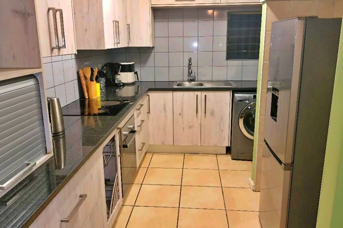 A functional kitchen featuring light wood-finish cabinetry, granite countertops, a tiled backsplash, and integrated space for laundry appliances.
