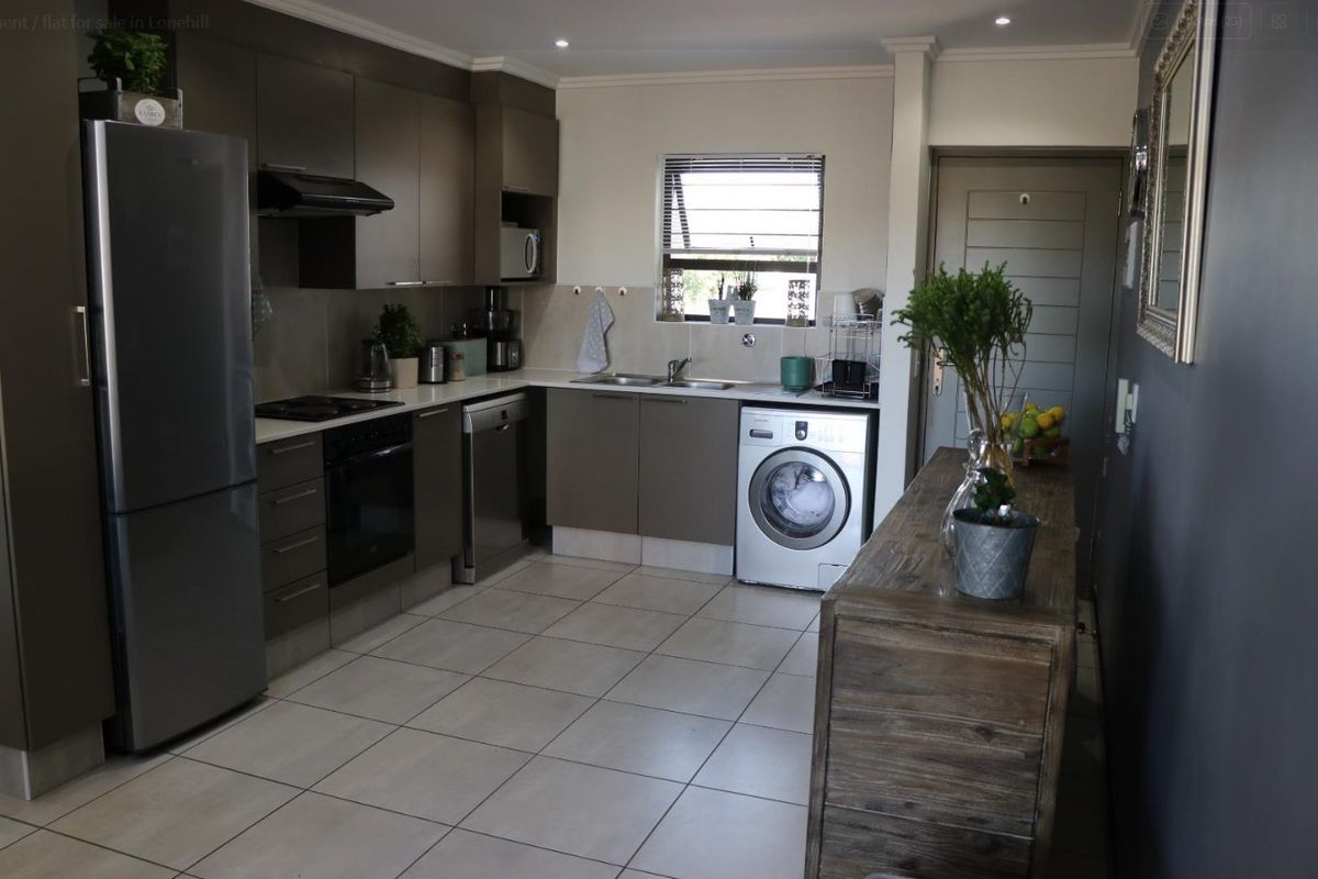 Modern kitchen featuring dark cabinetry, integrated appliances, tiled flooring, and a functional layout with ample counter space and natural light.