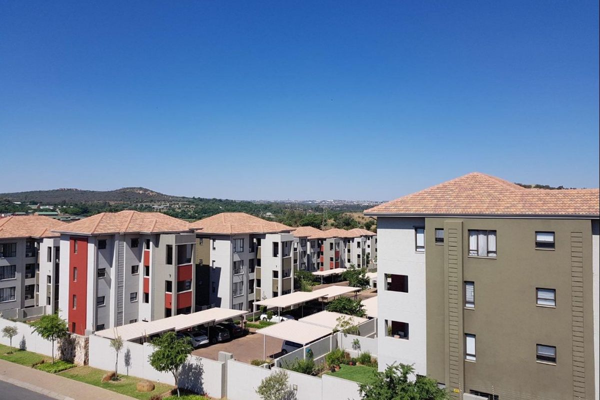 Aerial view of a modern apartment complex featuring multiple residential blocks, covered parking bays, and landscaped grounds under a clear sky.