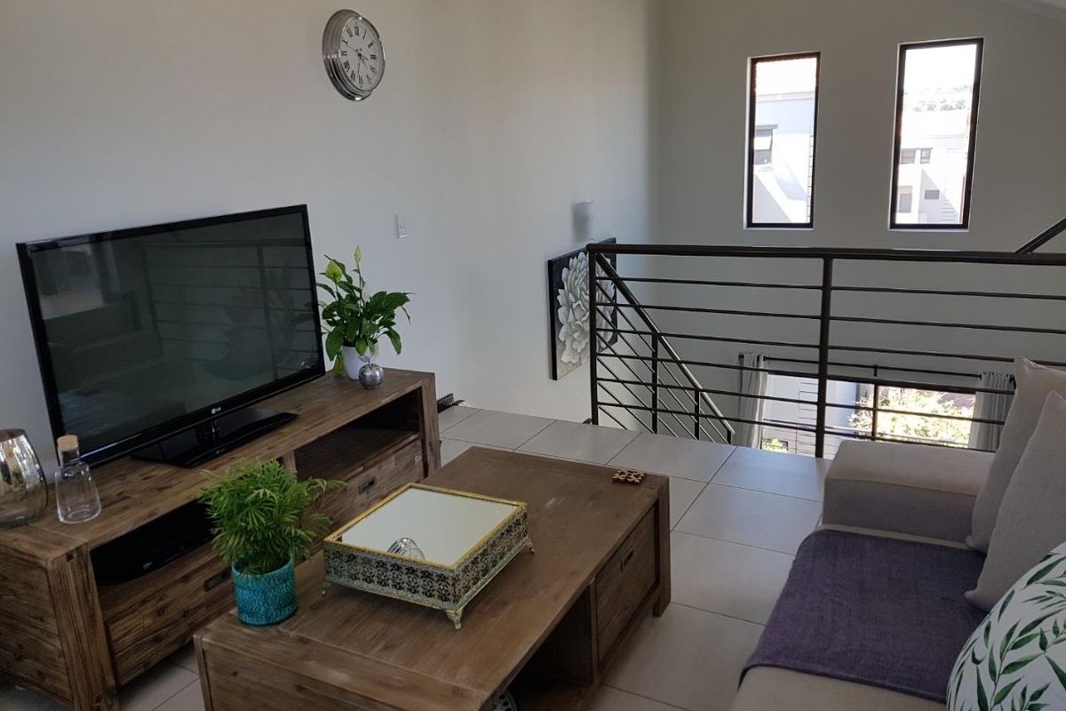 A bright living room featuring vaulted ceilings, tiled flooring, and a modern metal balustrade overlooking the lower level.
