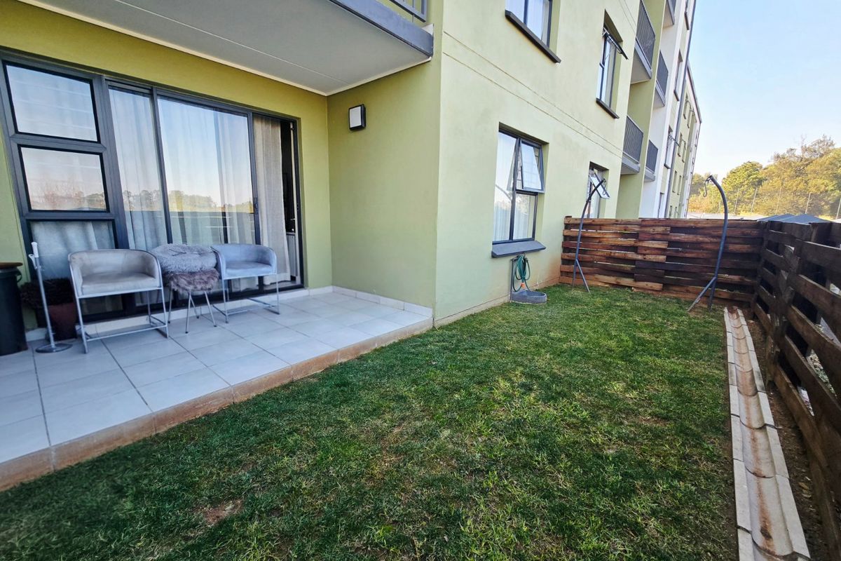 A ground floor apartment rear exterior featuring a tiled patio, sliding glass doors, and a private garden area with timber fencing.