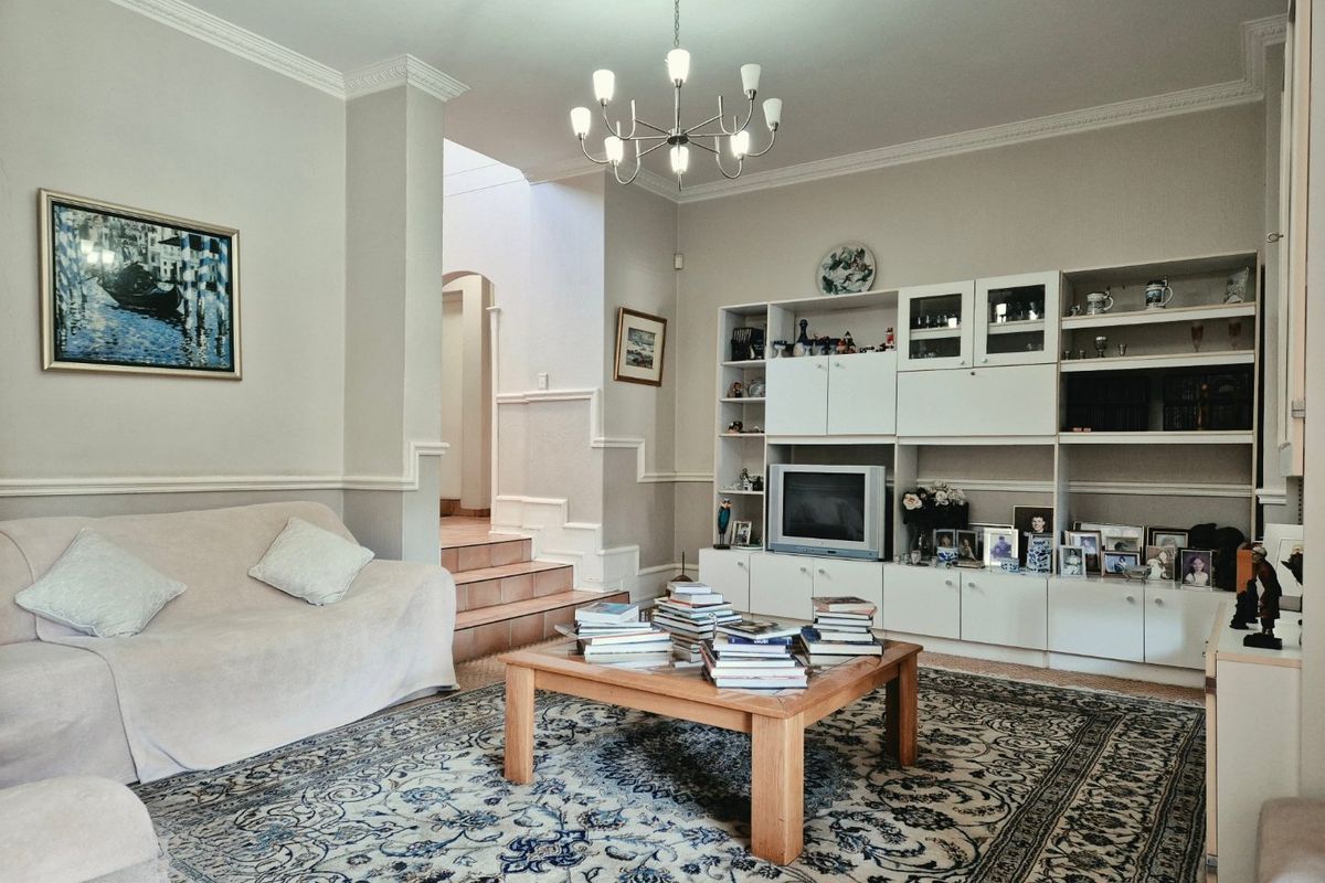 A spacious living room featuring classic crown molding, wainscoting, and extensive built-in cabinetry, with a tiled staircase leading to an upper level.