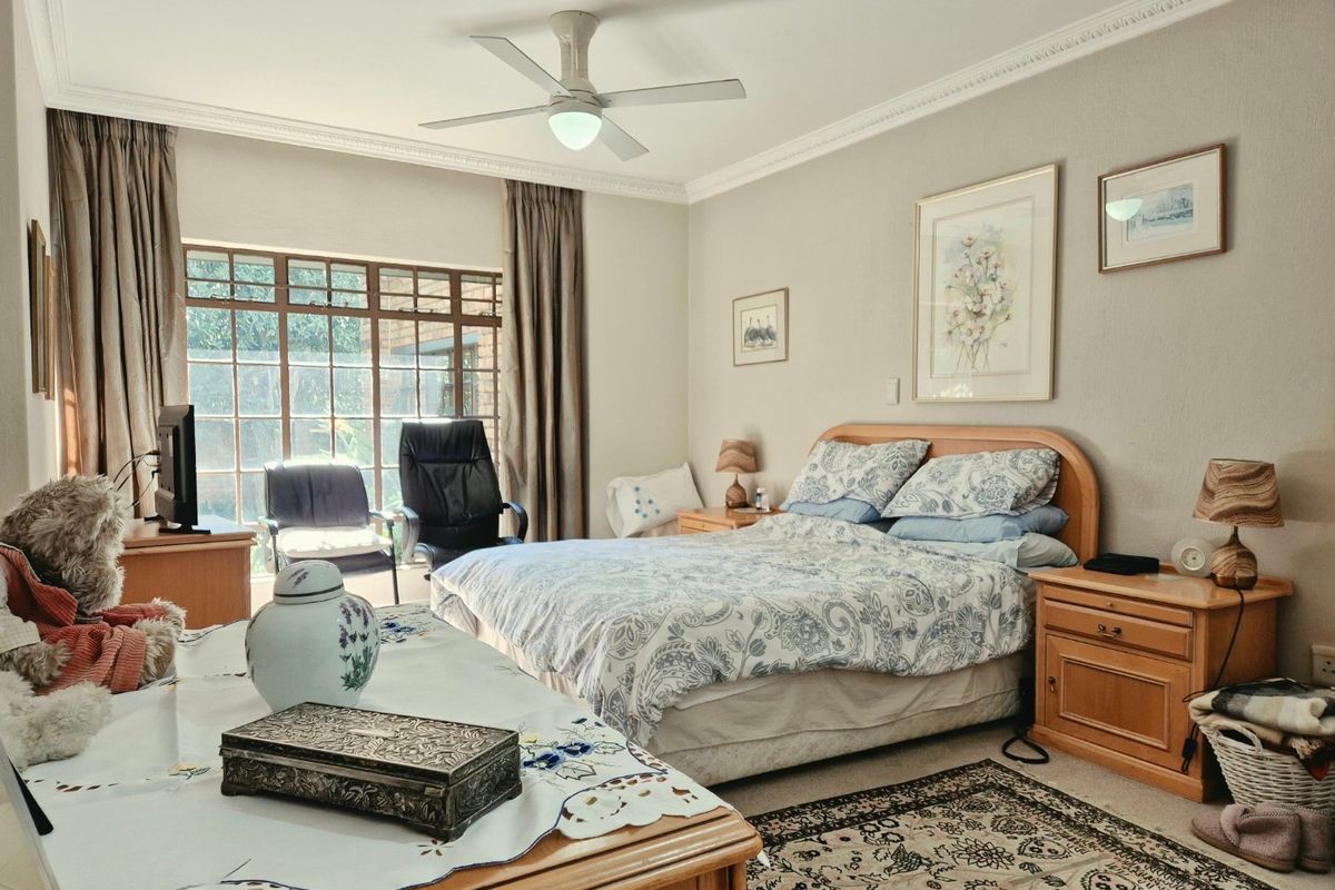 A spacious bedroom featuring crown molding, a ceiling fan, and a large window that provides natural light.