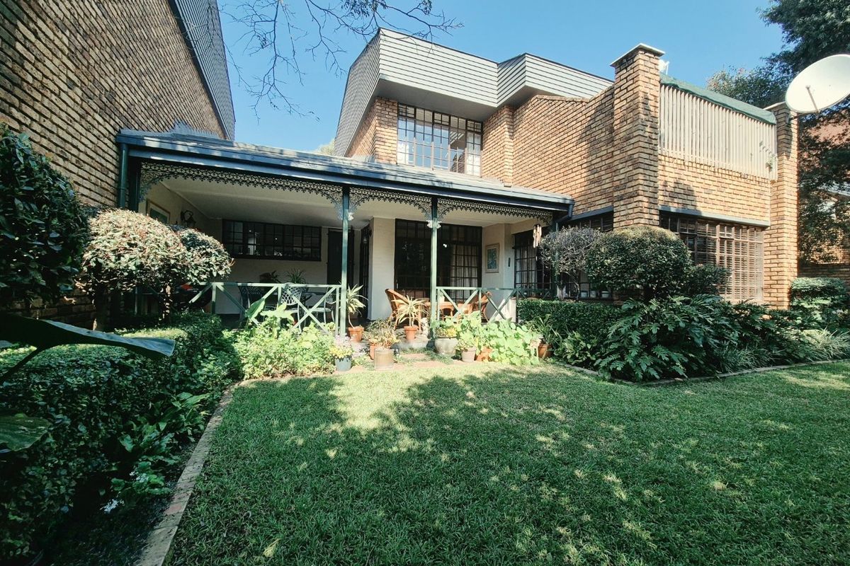 Rear view of the property featuring a brick facade, a covered patio with decorative ironwork, and a well-maintained garden.
