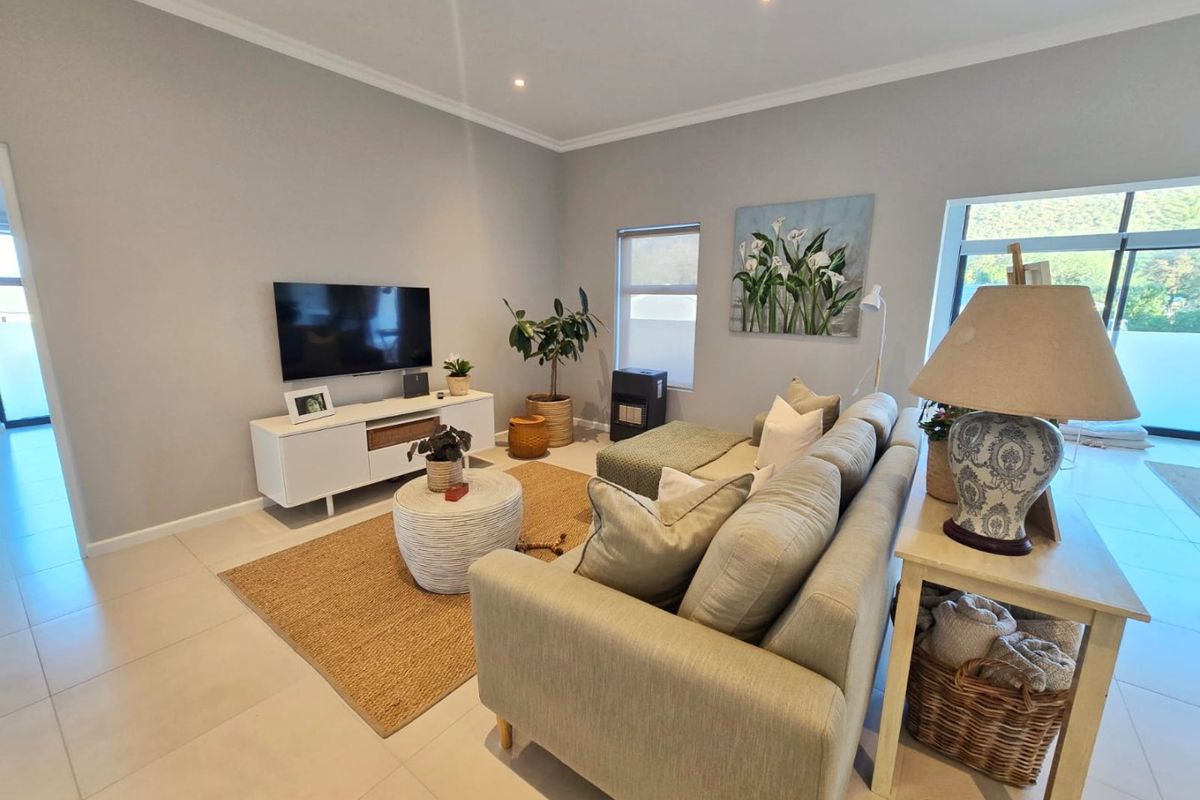 A bright and modern living room featuring neutral tiled flooring, recessed downlighting, and large windows that provide ample natural light.