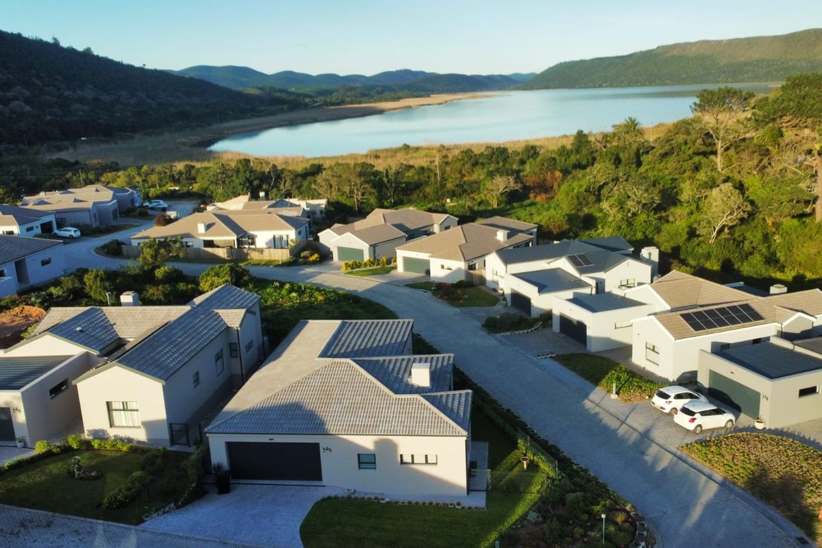 Aerial view of a modern residential estate featuring multiple homes with tiled roofs, solar panels, and paved driveways, set against a scenic landscape.