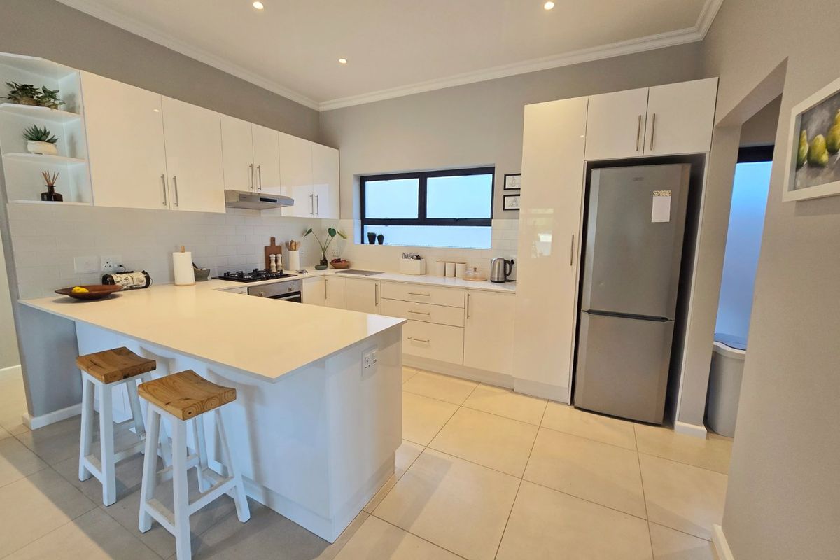 Modern kitchen featuring white high-gloss cabinetry, stone countertops, integrated appliances, and a breakfast bar island with tiled flooring and recessed lighting.