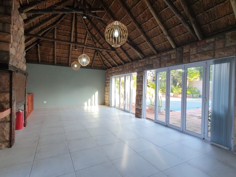 Spacious covered patio featuring a high thatched roof with exposed trusses, stone feature walls, built-in fireplace, and large stacker doors opening to the pool area.