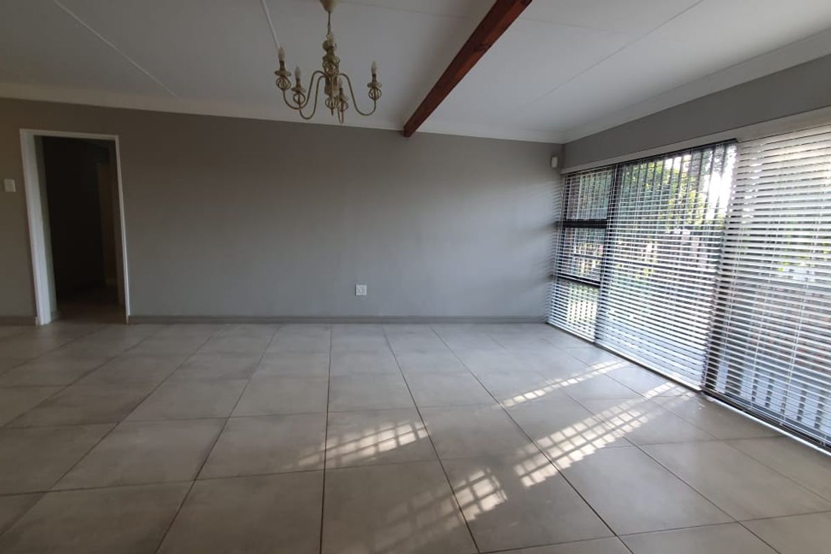 Spacious, light-filled living area featuring large sliding glass doors with venetian blinds, neutral tiled flooring, and an exposed ceiling beam.