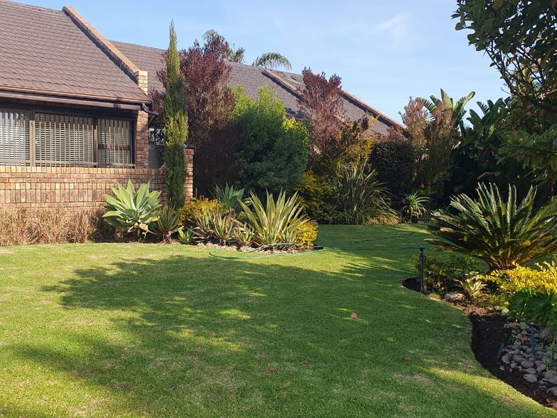 A well-maintained rear garden featuring a lush lawn, established landscaping, and a brick-clad house exterior with solar panels installed on the roof.