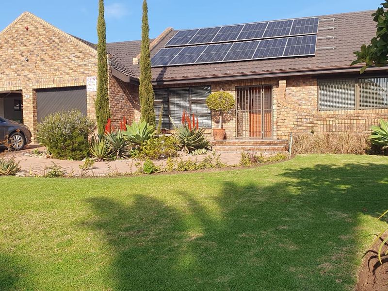 Front elevation of a brick house featuring a tiled roof with installed solar panels, a paved driveway, and a well-maintained front garden.