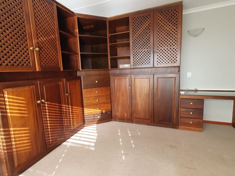 A dedicated home office space featuring extensive built-in wooden cabinetry, shelving, and a integrated desk area with neutral carpeting.