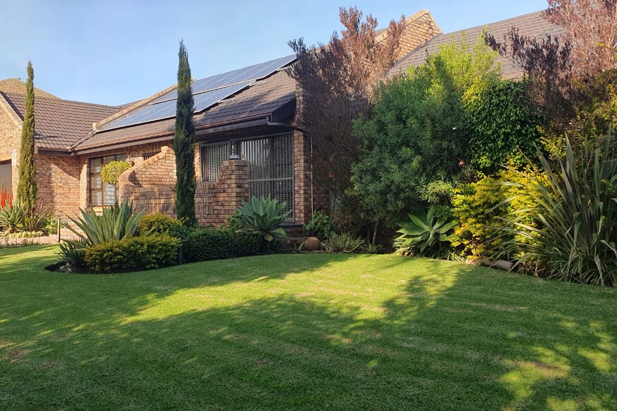 A well-maintained rear exterior view of a brick house featuring a lush green lawn, mature landscaping, and roof-mounted solar panels.