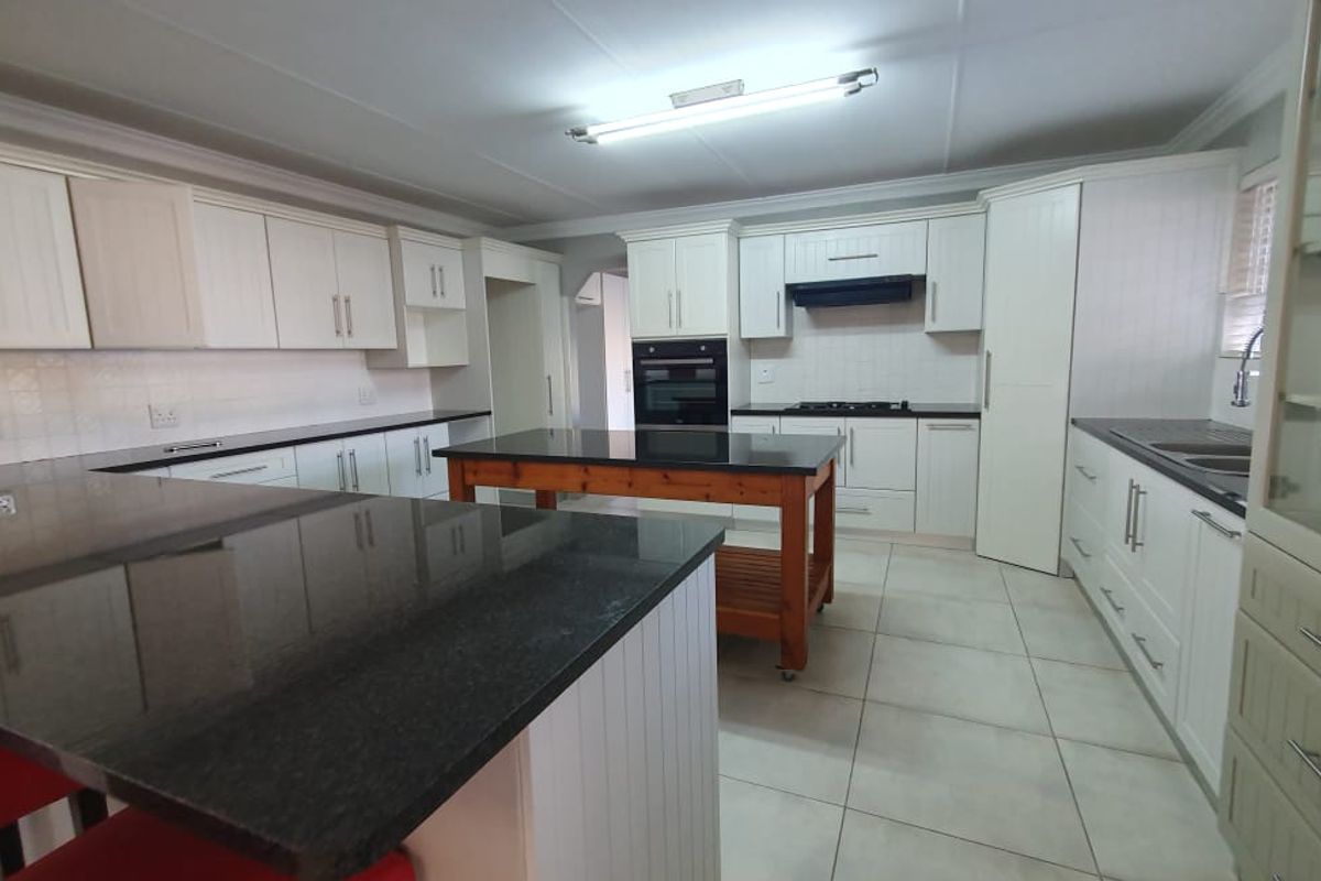 Spacious kitchen featuring white cabinetry, granite countertops, a central island, built-in oven, gas hob, and tiled flooring.