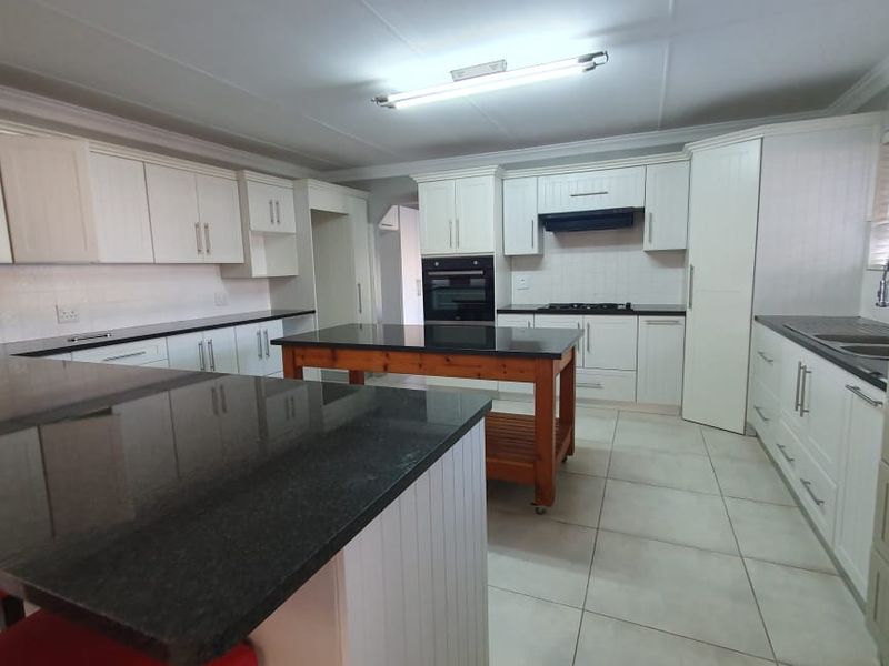 Spacious kitchen featuring white cabinetry, granite countertops, a central island, built-in oven, gas hob, and tiled flooring.