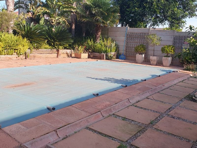 Outdoor pool area featuring a paved patio, retaining walls, and a swimming pool with a protective cover.