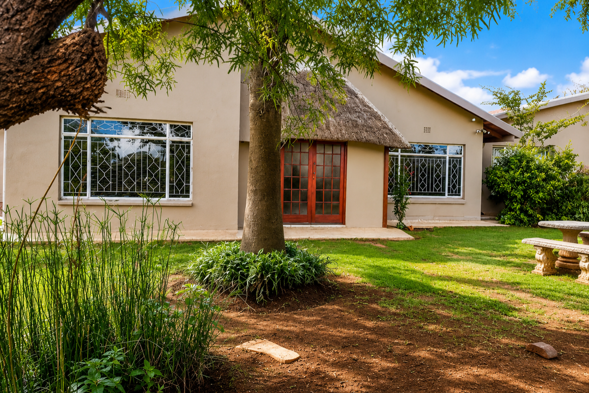 Rear view of the house featuring a thatched roof detail, security-barred windows, and a landscaped garden with a concrete seating area.