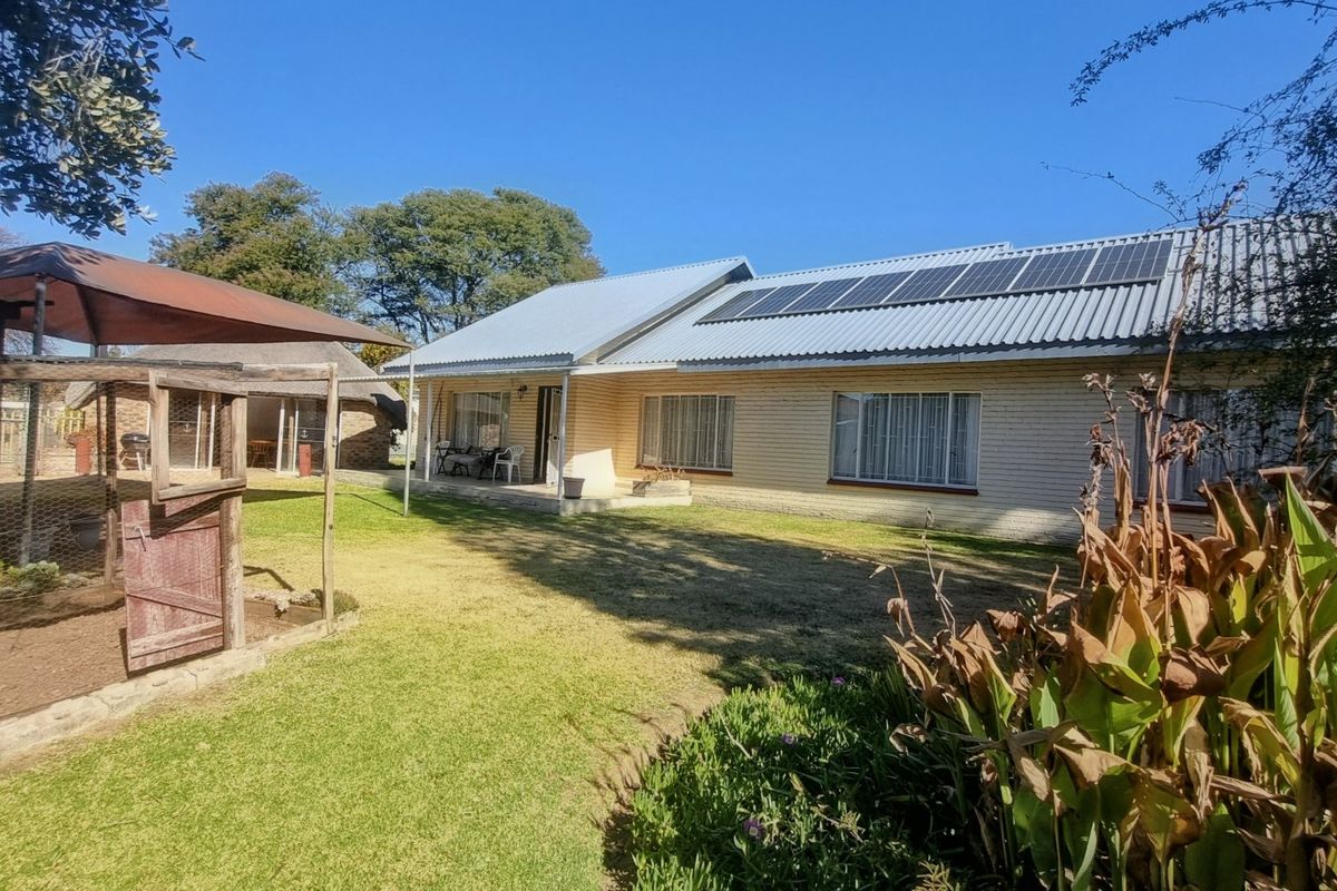 Rear view of the house featuring a brick facade, corrugated metal roof with installed solar panels, and a covered patio area overlooking the garden.