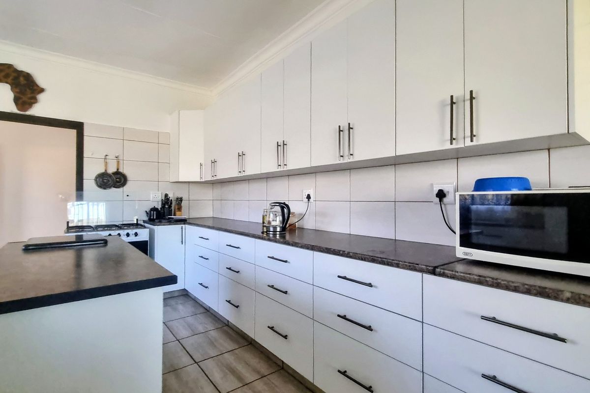 A functional kitchen featuring white cabinetry, dark laminate countertops, tiled backsplash, and built-in appliances including a microwave and gas stove.