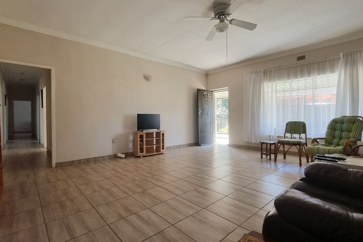 A spacious living room featuring neutral tiled flooring, a ceiling fan, and direct access to the exterior through a security gate.