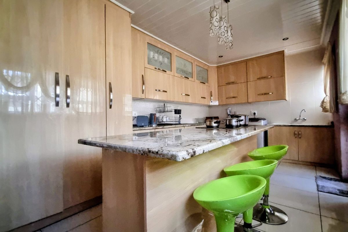 A functional kitchen featuring light wood cabinetry, granite countertops, a breakfast bar, and tiled flooring.
