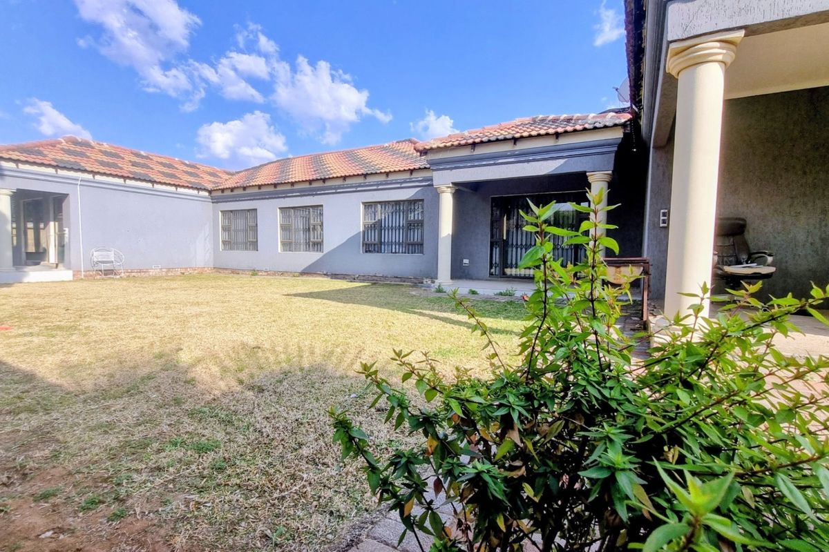 Rear view of the house featuring a covered patio area, tiled roof, and a spacious garden with established lawn.