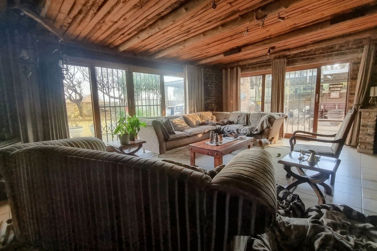 Spacious living room featuring rustic exposed timber beam ceilings, exposed brick walls, and large sliding glass doors providing access to the garden.