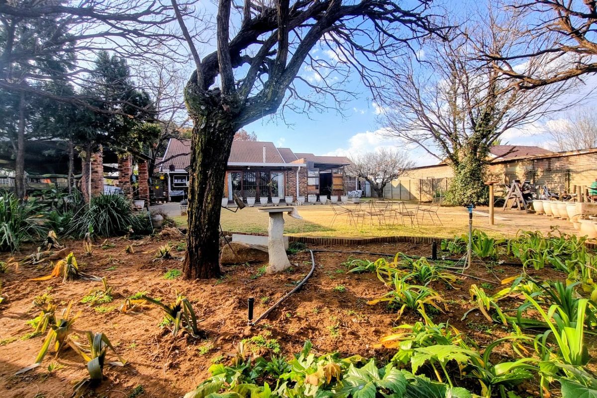 A spacious rear garden featuring a lawn, mature trees, and a brick-built house with a tiled roof and paved patio area.
