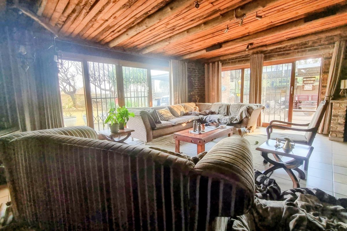 Spacious living room featuring exposed timber beam ceilings, rustic brick walls, tiled flooring, and large sliding glass doors providing access to the outdoor area.