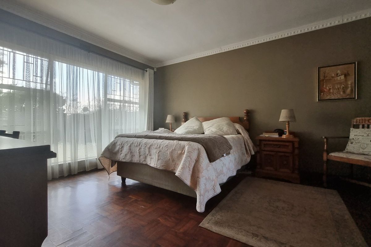 A spacious bedroom featuring classic parquet flooring, decorative ceiling cornicing, and large windows fitted with security gates for added peace of mind.