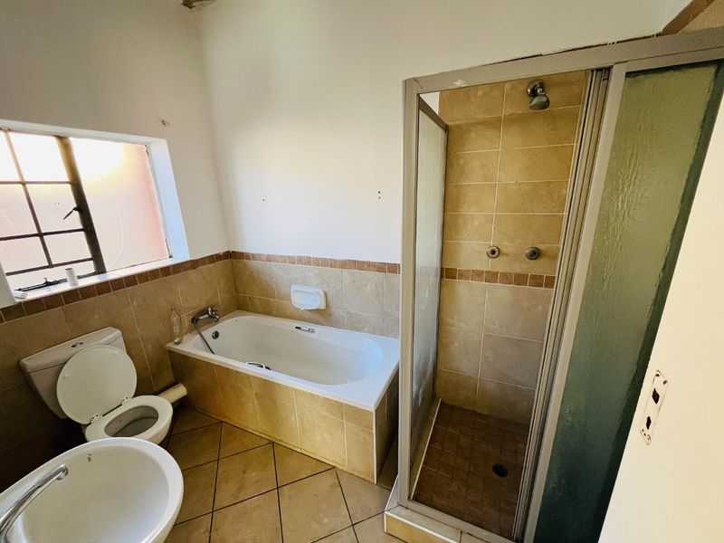 A functional bathroom featuring a built-in bathtub, separate shower enclosure, pedestal basin, and toilet with neutral tiled finishes.
