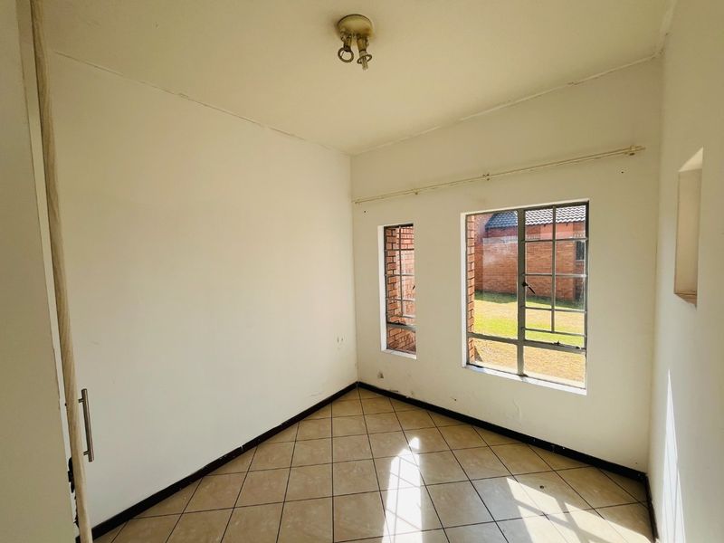 An empty bedroom featuring tiled flooring and steel-framed windows, offering a blank canvas for potential interior design updates.