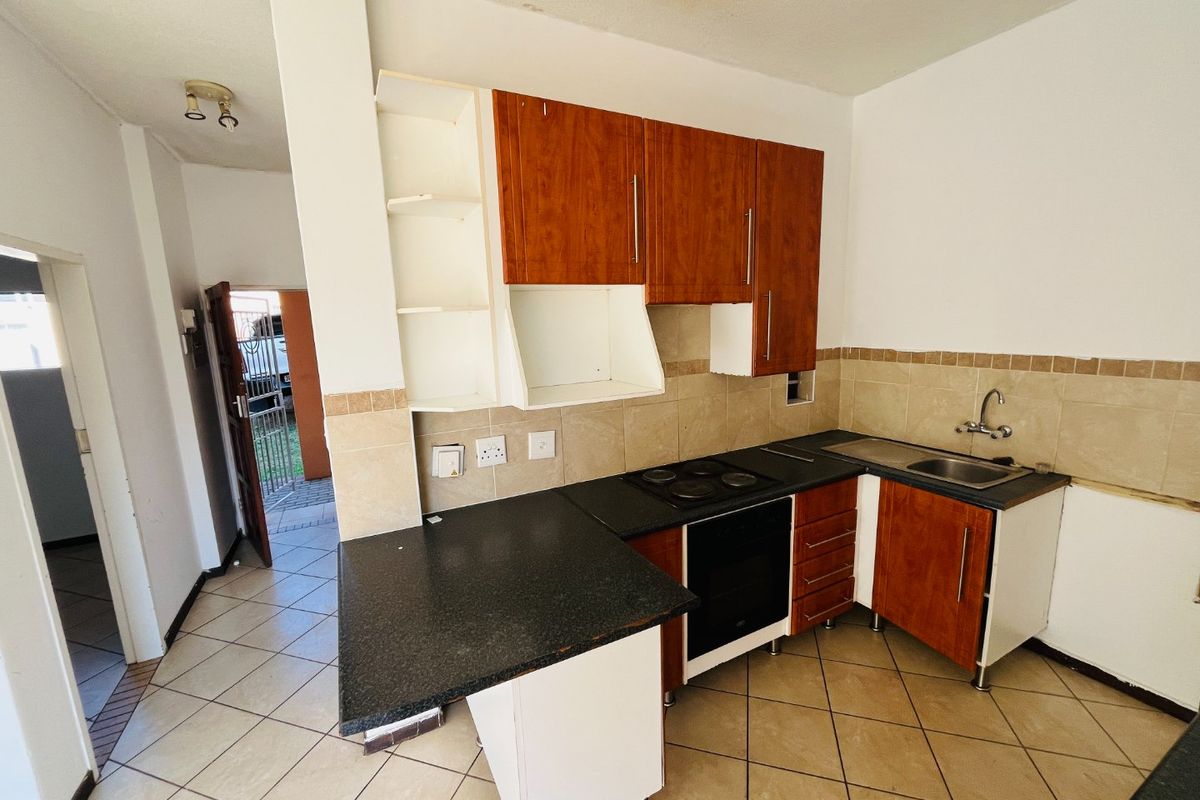 A compact kitchen featuring built-in cabinetry, an electric hob, oven, and tiled backsplash, requiring some cosmetic updates to restore its functionality and appeal.