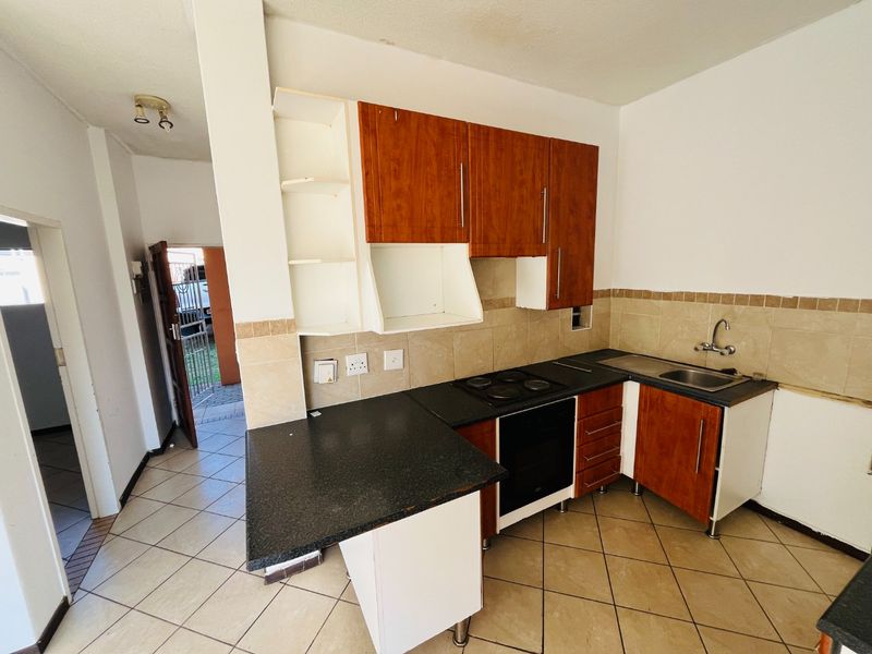 A compact kitchen featuring built-in cabinetry, an electric hob, oven, and tiled backsplash, requiring some cosmetic updates to restore its functionality and appeal.