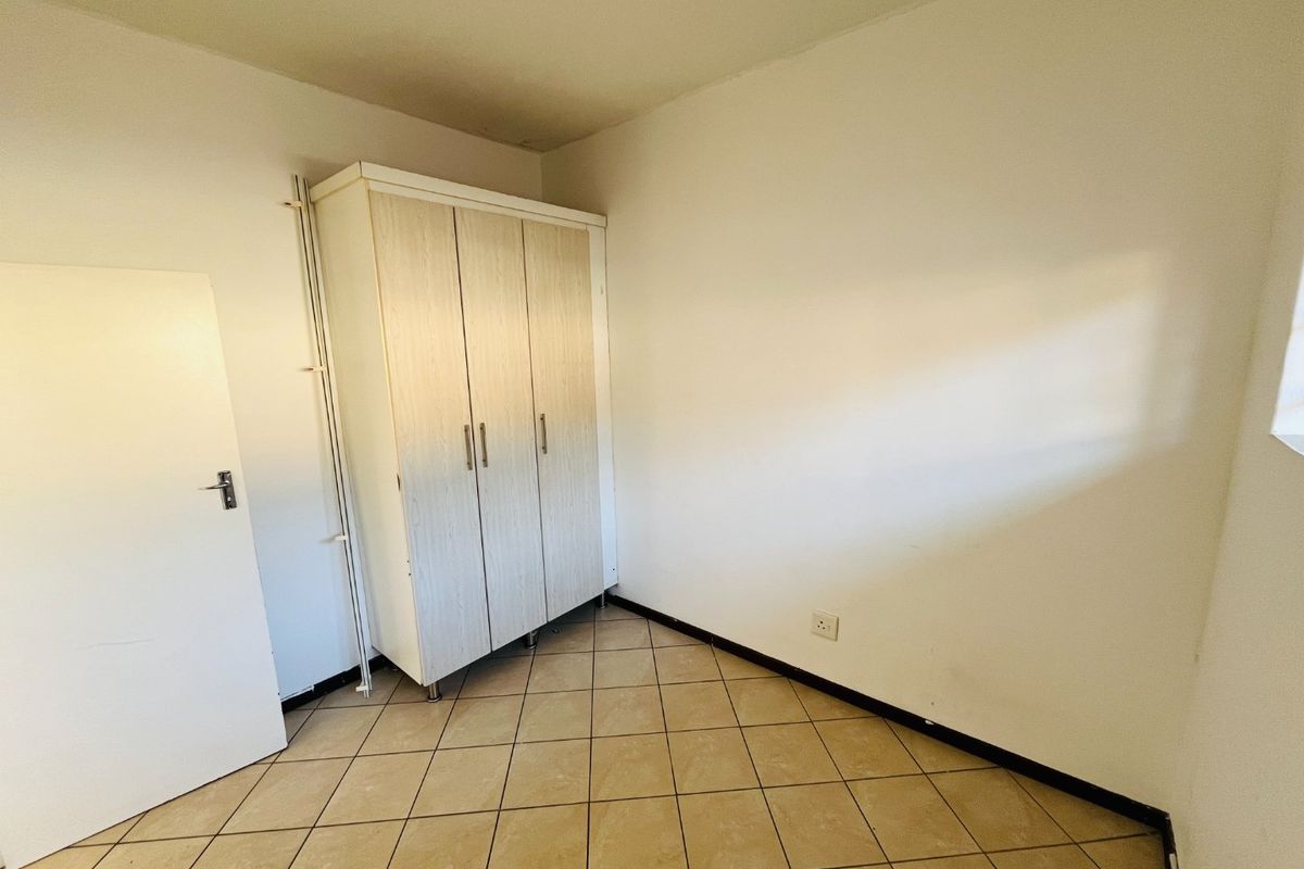 A simple, empty bedroom featuring tiled flooring and a built-in wardrobe, offering a blank canvas for personalization.