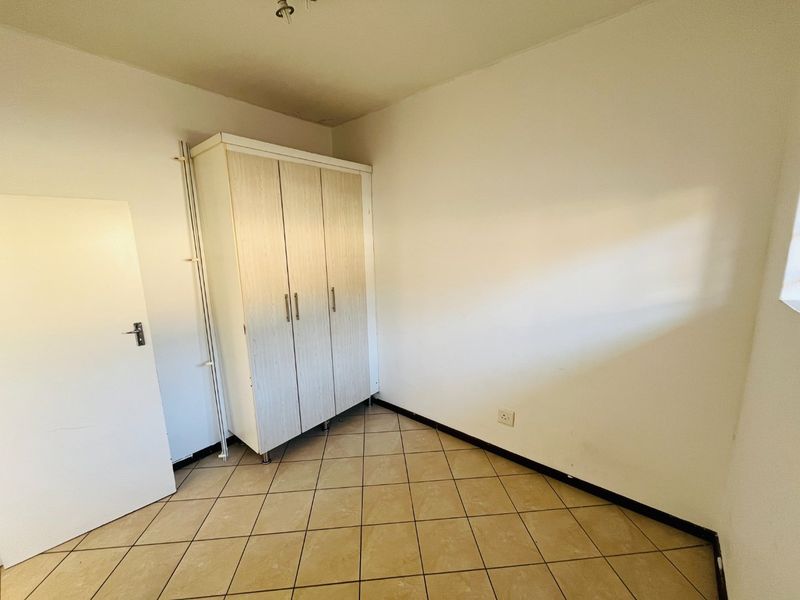 A simple, empty bedroom featuring tiled flooring and a built-in wardrobe, offering a blank canvas for personalization.