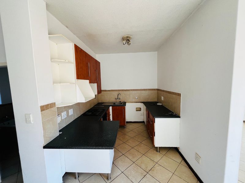 A dated kitchen featuring built-in cabinetry, dark laminate countertops, and ceramic tile flooring, currently requiring cosmetic updates and appliance installation.