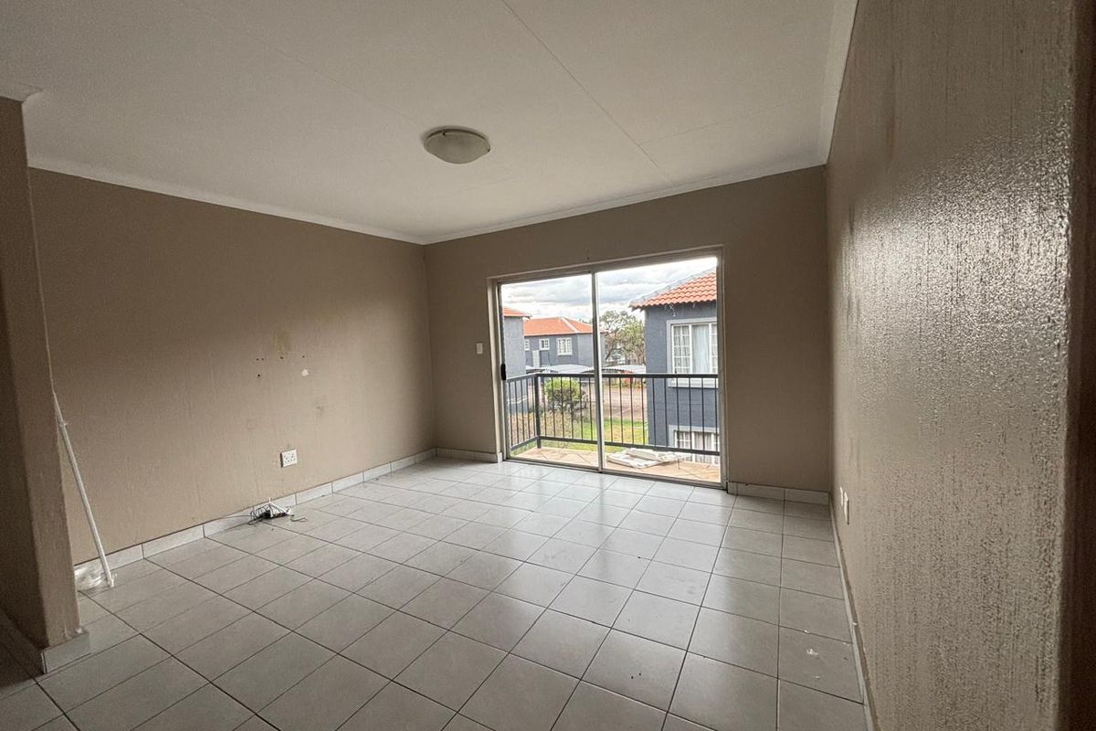 An empty living room featuring tiled flooring and a sliding glass door leading to a small balcony.