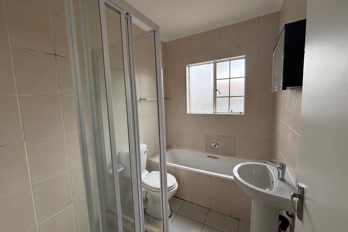 A functional bathroom featuring a separate shower enclosure, bathtub, pedestal basin, and toilet with neutral wall and floor tiling.