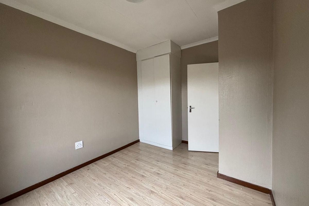 A vacant bedroom featuring light-toned laminate flooring, neutral wall paint, and a built-in white wardrobe.