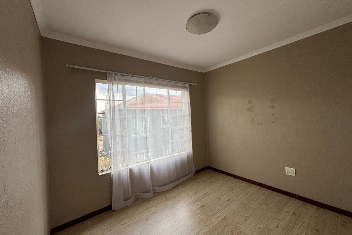 An empty bedroom featuring laminate flooring, a ceiling light fixture, and a window with a curtain rod. The walls show signs of surface wear.