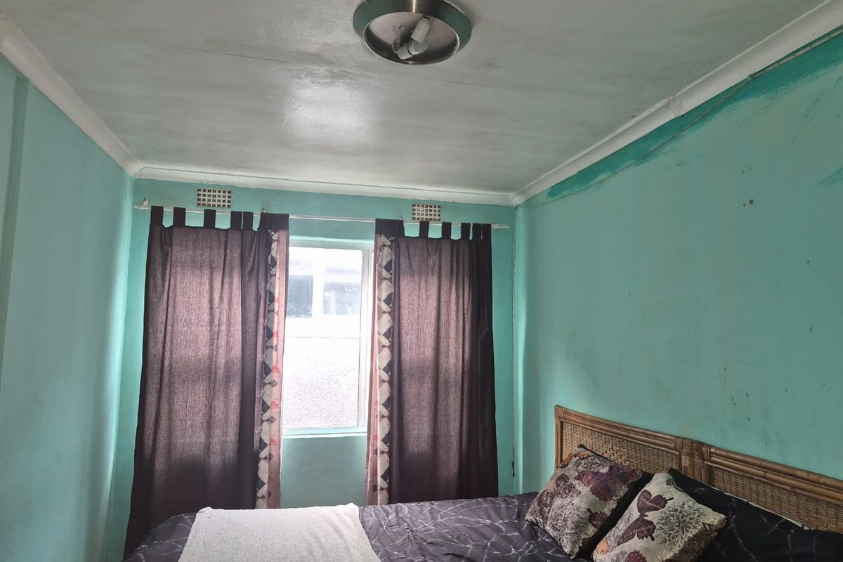 A bedroom featuring a window and ceiling light fixture, currently requiring cosmetic updates to the wall finishes.